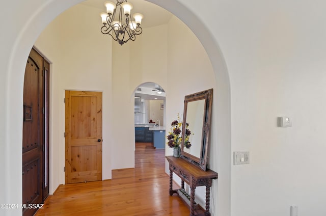 hall featuring light wood-type flooring, an inviting chandelier, a high ceiling, and arched walkways