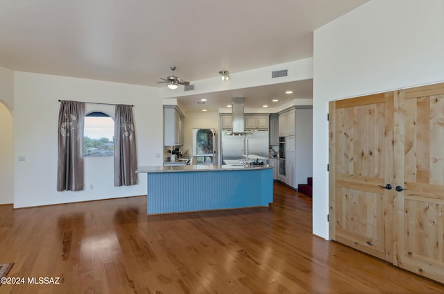 kitchen featuring dark hardwood / wood-style floors, gray cabinets, kitchen peninsula, ceiling fan, and wall chimney range hood