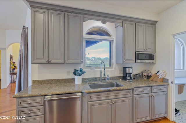 kitchen with arched walkways, stone countertops, gray cabinetry, stainless steel appliances, and a sink