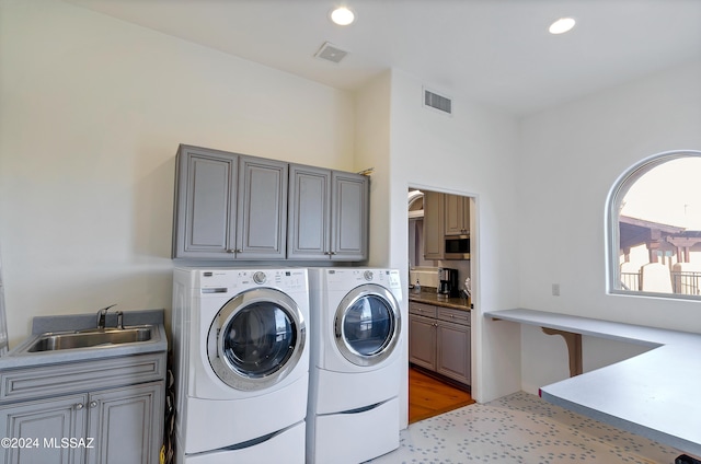 clothes washing area with cabinets, sink, washer and clothes dryer, and light hardwood / wood-style flooring