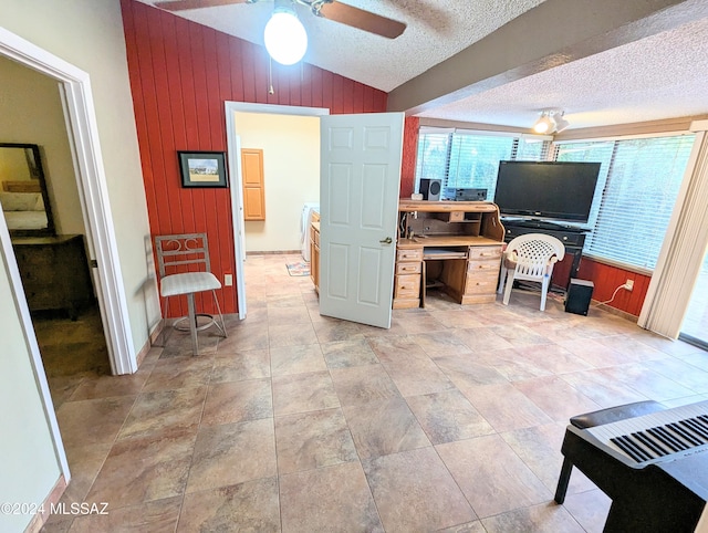 interior space featuring lofted ceiling, ceiling fan, wooden walls, and a textured ceiling