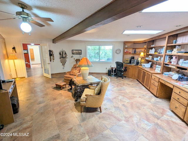 living room with beamed ceiling, a textured ceiling, built in desk, and ceiling fan