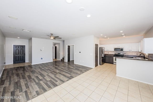 kitchen with backsplash, white cabinets, ceiling fan, light wood-type flooring, and appliances with stainless steel finishes