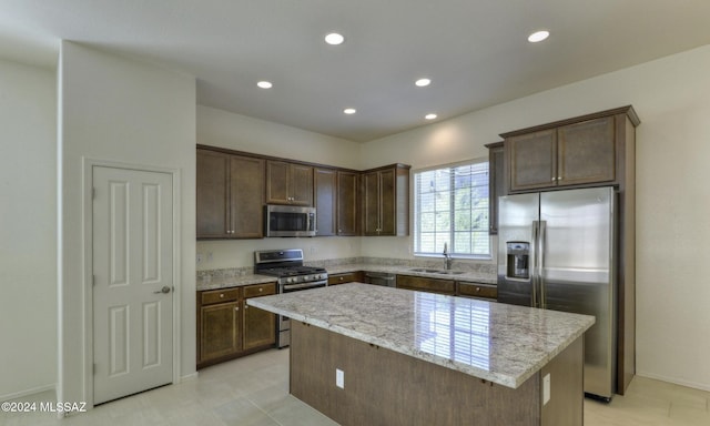 kitchen with sink, light stone countertops, a kitchen island, dark brown cabinetry, and stainless steel appliances