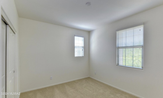 unfurnished bedroom featuring a closet, light colored carpet, and multiple windows