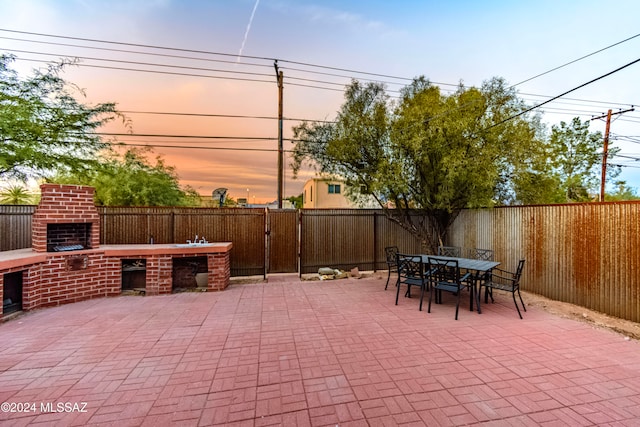 patio terrace at dusk featuring a fireplace and an outdoor kitchen