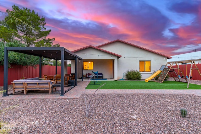 back house at dusk featuring a patio area and a playground