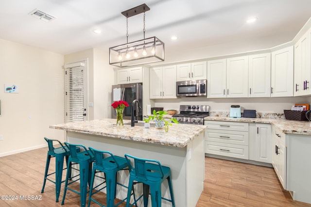 kitchen featuring appliances with stainless steel finishes, a center island with sink, decorative light fixtures, and light hardwood / wood-style floors