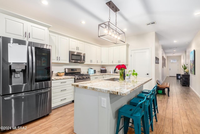 kitchen featuring light stone countertops, stainless steel appliances, decorative light fixtures, white cabinets, and light wood-type flooring