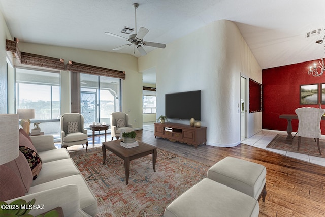 living room with lofted ceiling, ceiling fan with notable chandelier, plenty of natural light, and light wood-type flooring