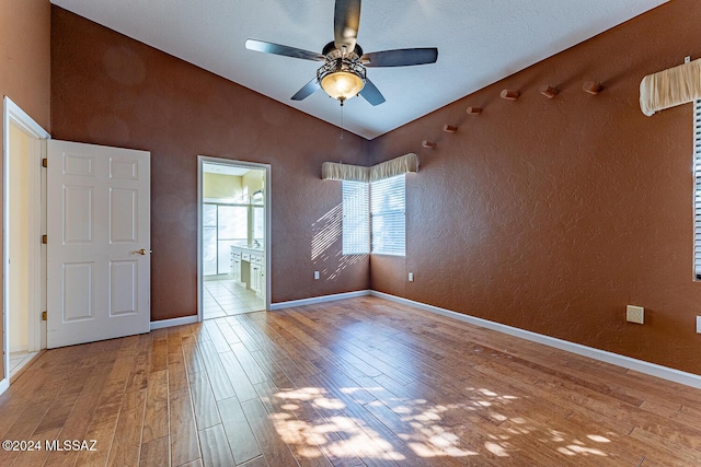 unfurnished bedroom with hardwood / wood-style floors, lofted ceiling, connected bathroom, and ceiling fan