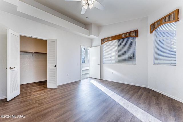 unfurnished bedroom featuring dark wood-type flooring, ceiling fan, multiple windows, and a closet