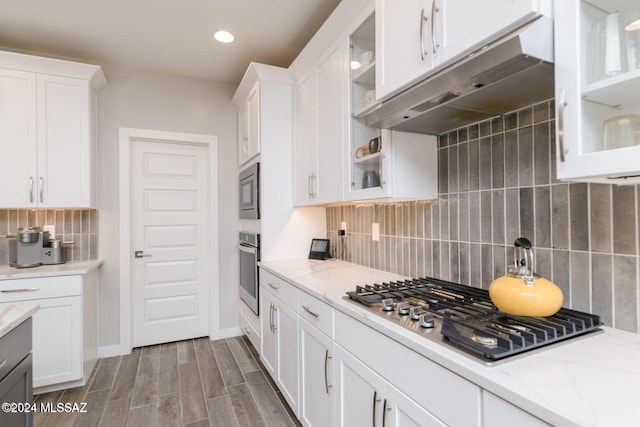 kitchen featuring hardwood / wood-style floors, white cabinets, light stone countertops, appliances with stainless steel finishes, and tasteful backsplash