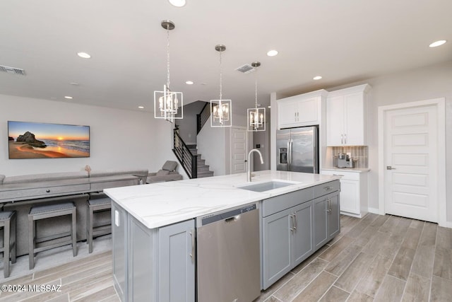 kitchen with a center island with sink, hanging light fixtures, sink, and appliances with stainless steel finishes