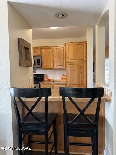 kitchen with kitchen peninsula, light brown cabinetry, black range, and a breakfast bar area