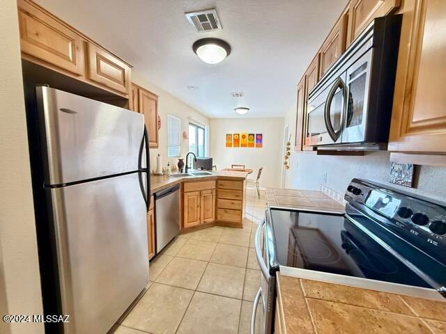 kitchen with stainless steel appliances, sink, light brown cabinets, tile counters, and light tile patterned flooring