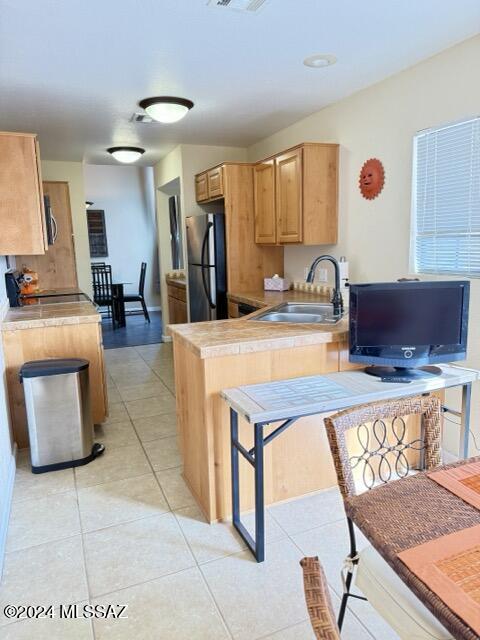 kitchen with light brown cabinetry, stainless steel fridge, sink, and light tile patterned flooring