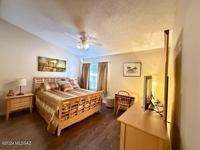 bedroom with a textured ceiling, vaulted ceiling, ceiling fan, and dark wood-type flooring