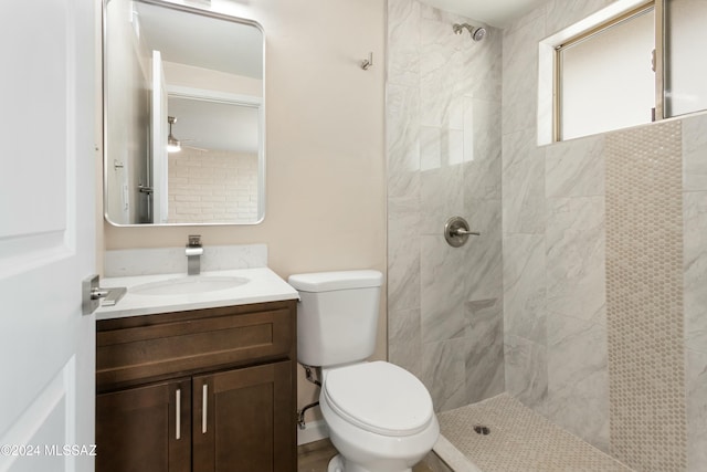 bathroom featuring a tile shower, ceiling fan, vanity, and toilet