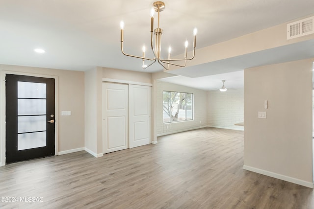 interior space with ceiling fan with notable chandelier, light hardwood / wood-style flooring, and brick wall