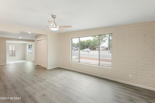 empty room with ceiling fan, brick wall, and light wood-type flooring