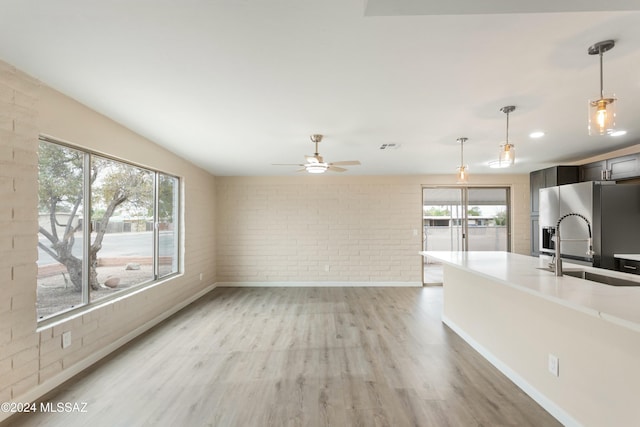 kitchen featuring stainless steel refrigerator with ice dispenser, brick wall, sink, pendant lighting, and light hardwood / wood-style floors