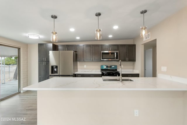 kitchen with pendant lighting, light stone counters, stainless steel appliances, and light hardwood / wood-style flooring