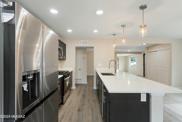 kitchen with appliances with stainless steel finishes, sink, decorative light fixtures, light hardwood / wood-style floors, and an island with sink