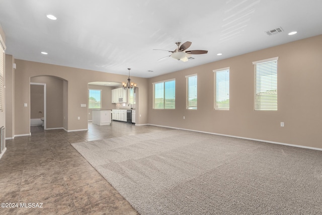 unfurnished living room featuring ceiling fan with notable chandelier, carpet floors, and a healthy amount of sunlight