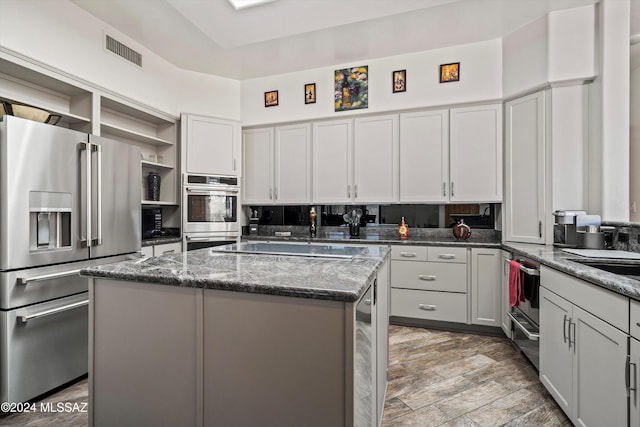 kitchen featuring gray cabinetry, dark stone counters, light wood-type flooring, a kitchen island, and stainless steel appliances