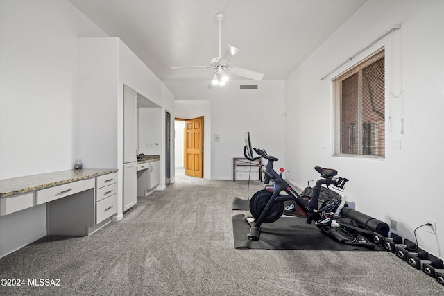 exercise area featuring ceiling fan, built in desk, and light carpet