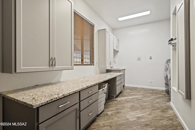 clothes washing area featuring hardwood / wood-style flooring, washer and clothes dryer, and cabinets