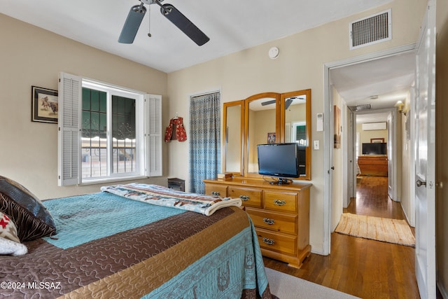 bedroom featuring dark hardwood / wood-style flooring, a wall unit AC, and ceiling fan