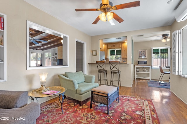 living room featuring wood-type flooring, an AC wall unit, a healthy amount of sunlight, and beam ceiling