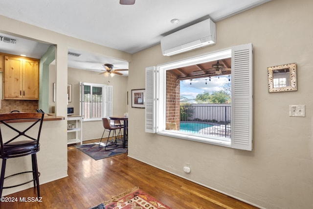 interior space with light brown cabinets, an AC wall unit, a wealth of natural light, and dark wood-type flooring