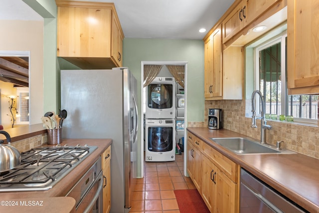 kitchen featuring sink, appliances with stainless steel finishes, tasteful backsplash, stacked washer / drying machine, and light tile patterned flooring