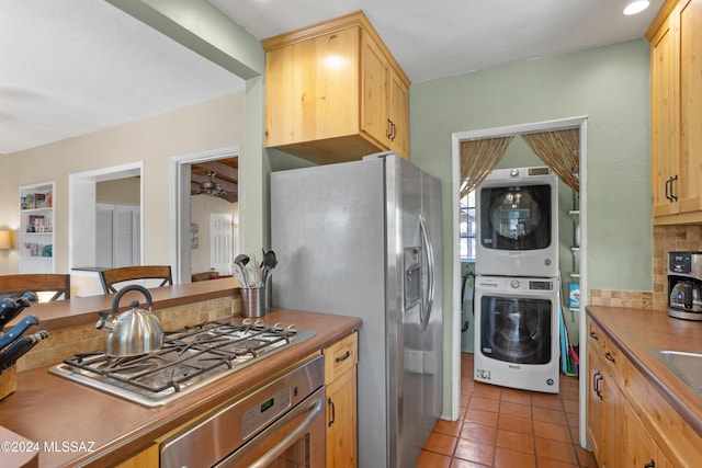 kitchen featuring light brown cabinetry, appliances with stainless steel finishes, backsplash, and stacked washer and clothes dryer