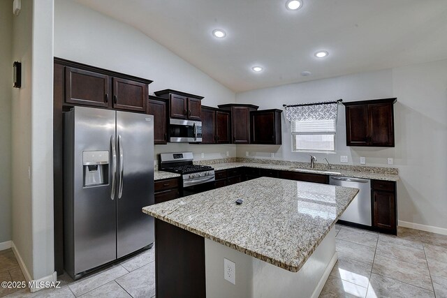 kitchen featuring a center island, appliances with stainless steel finishes, a sink, dark brown cabinetry, and light stone countertops