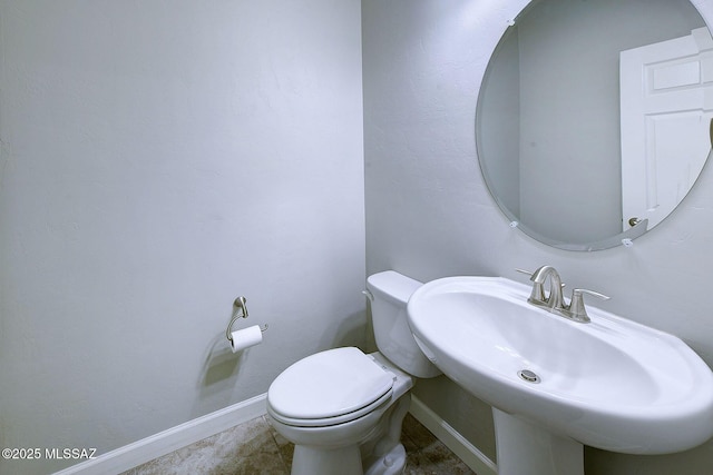 half bath with toilet, baseboards, and a sink