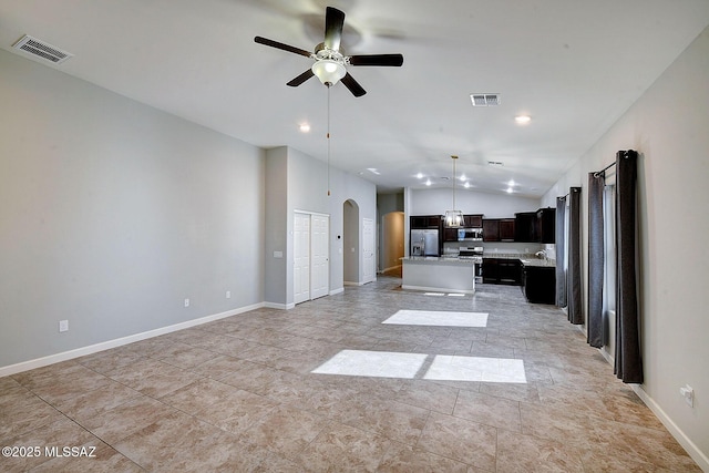 kitchen featuring arched walkways, stainless steel appliances, a kitchen island, open floor plan, and light countertops