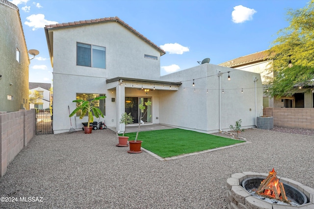 back of property with central AC, a fire pit, a patio area, and a lawn