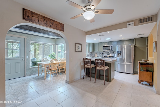 kitchen with ceiling fan, stainless steel appliances, backsplash, a breakfast bar, and light tile patterned floors