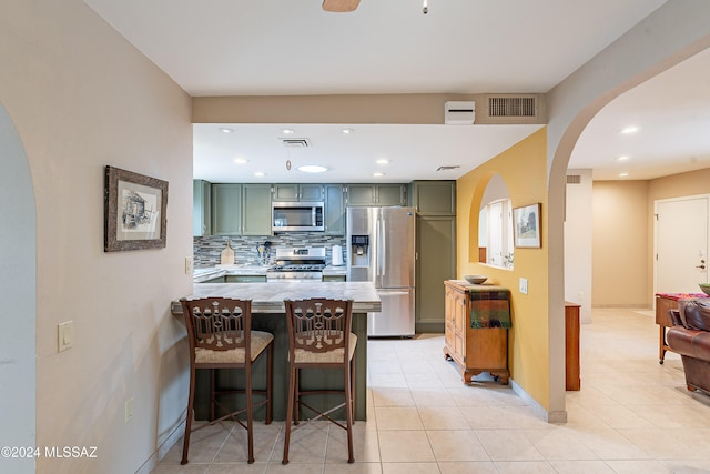 kitchen featuring a kitchen bar, appliances with stainless steel finishes, kitchen peninsula, tasteful backsplash, and green cabinets