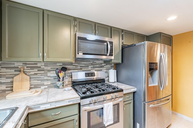 kitchen featuring backsplash, green cabinets, light tile patterned floors, and appliances with stainless steel finishes