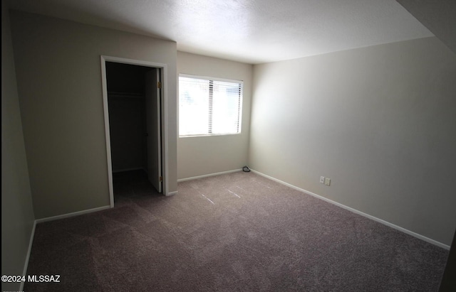 unfurnished bedroom featuring dark colored carpet, a walk in closet, and a closet