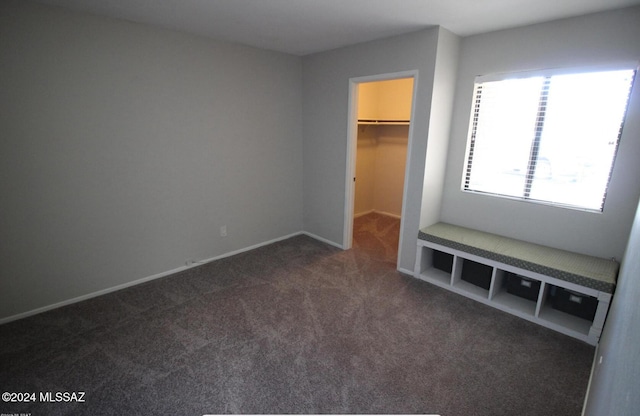 unfurnished bedroom with a walk in closet, a closet, and dark carpet