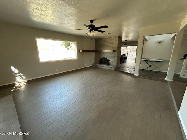 unfurnished living room featuring wood-type flooring, a textured ceiling, a brick fireplace, and ceiling fan