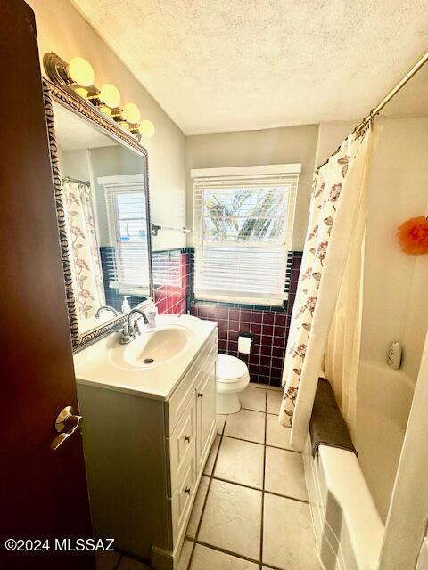 full bathroom with tile patterned flooring, a wealth of natural light, vanity, and tile walls