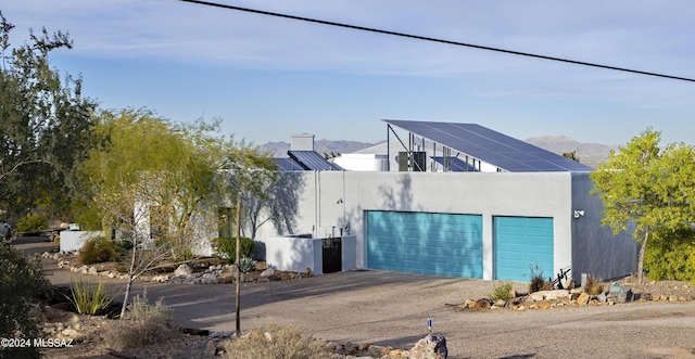 exterior space with aphalt driveway, solar panels, stucco siding, an attached garage, and a mountain view