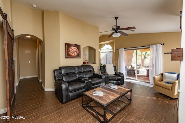 living room featuring ceiling fan, a barn door, dark wood-type flooring, and vaulted ceiling